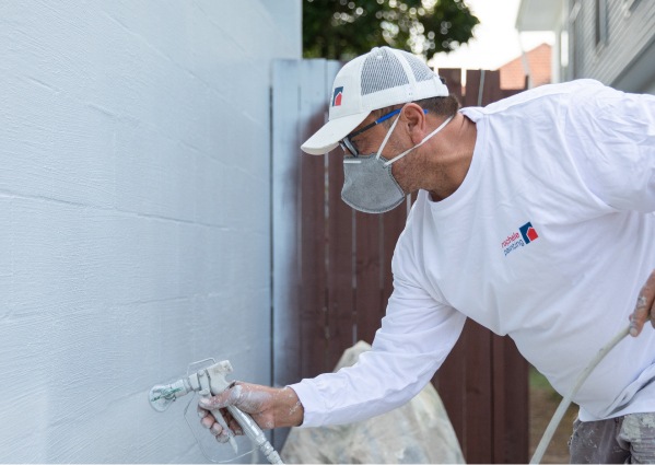 exterior house painter spraying paint on wall